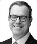 A person wearing glasses and a suit  Description automatically generated